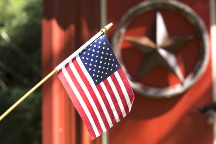 Small American Flag waving; in the background, a metal star hanging on a red shed 