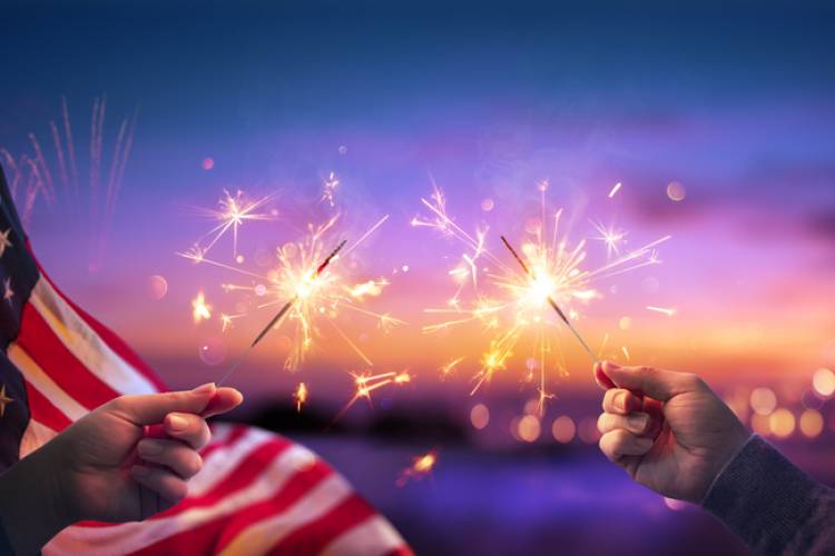 forth of july sparklers with american flag and sun set in background