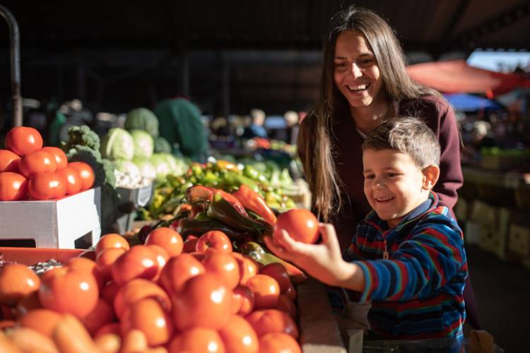 mother and son at farmers market picking up tomatoes and other veggies