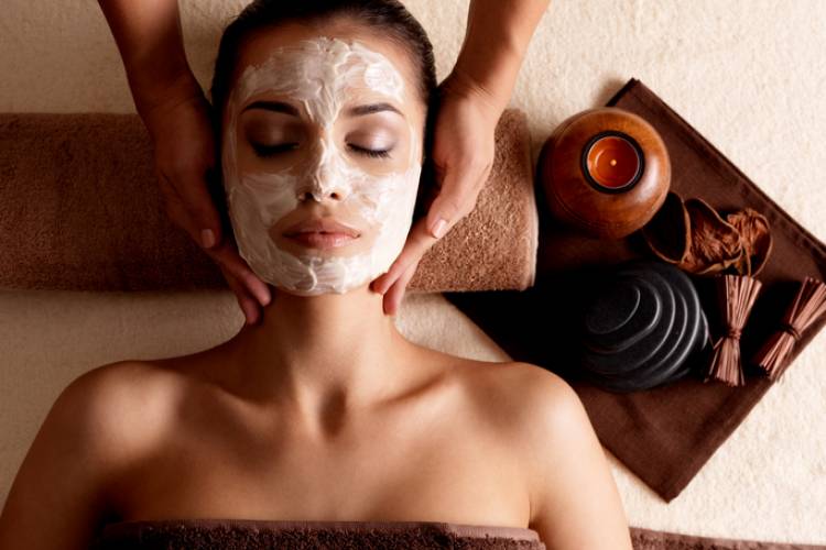 A woman at a spa has her neck massaged while she has a facial treatment